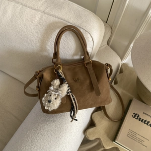 Détail du sac Boston marron foncé avec breloque lapin en peluche et logo de marque gravé
