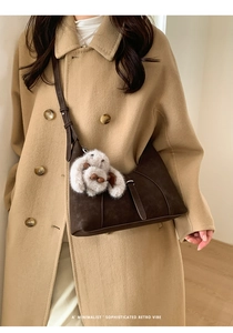 Detail of dark brown suede crossbody bag with a cute plush bunny charm on a beige coat