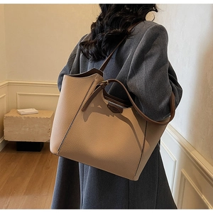 Detail of large beige tote bag with brown straps and lychee texture on grey blazer