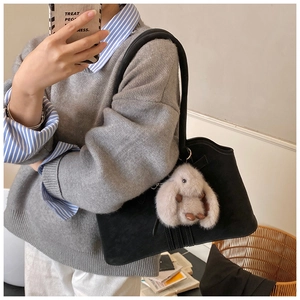 Detail of a black suede tote bag with a soft beige plush rabbit charm for daily use