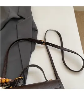 Détail de la bandoulière réglable avec boucle en métal et breloque perlée sur un sac marron