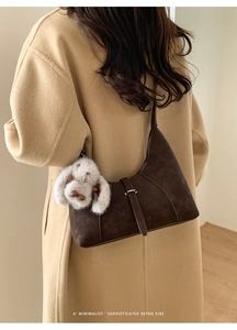 Detail of dark brown suede crescent bag with metal buckle and plush bunny charm on model