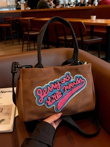 Sac à main en peluche marron avec broderie Jerry et bandoulière noire dans un café
