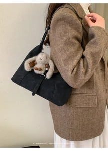 Detail of black suede half-moon bag featuring a plush rabbit charm on a stylish model