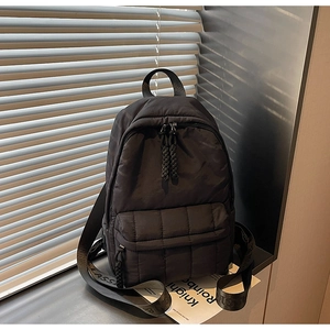 Detail of black quilted nylon backpack featuring checkered texture and woven handles