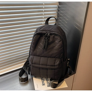 Macro detail of black quilted nylon backpack featuring branded straps and woven pullers