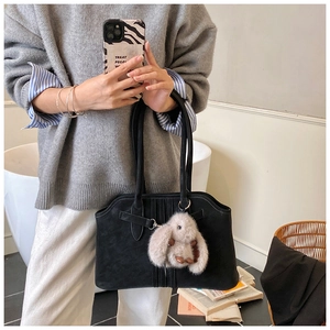 Close-up of black suede tote bag with a beige plush bunny pendant in a home setting