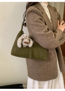 Olive green suede shoulder bag shown with white plush rabbit charm on a brown blazer outfit