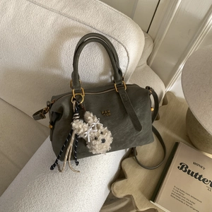 Sac à main bowling vert olive foncé avec logo doré et charm lapin en peluche sur canapé