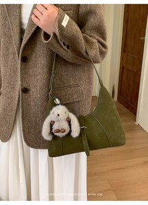 Dunkelgrüne Wildleder-Schultertasche mit Plüschhasen-Anhänger über einem Fischgrät-Blazer