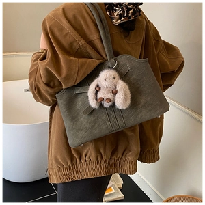 Detail of dark green leather tote bag with fluffy bunny charm on a casual outfit