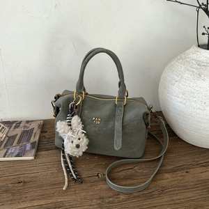 Détail du sac Boston vert-gris avec ferrures dorées, logo et breloque chiot en peluche