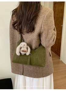 Detail of olive green suede hobo bag with stitching and plush bunny charm on a model