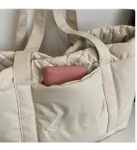 Close-up of beige quilted tote bag showing the front zipper pocket with a pink wallet