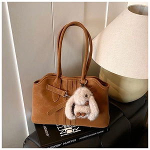 Detailed macro view of the brown suede tote bag with a plush grey bunny charm and leather straps