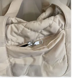 Detail of silver zipper and diamond quilted texture on beige nylon shoulder bag