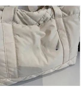 Detail of off-white quilted nylon shoulder bag showing soft puffer texture and embroidery