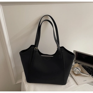 Detail of black pebbled leather tote bag with zip closure and laptop on desk