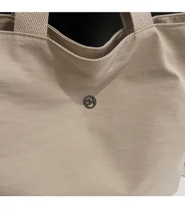 Detail of beige tote bag featuring a round gunmetal logo buckle and woven texture