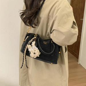 Détail du sac bowling noir avec logo doré et breloque lapin en peluche sur manteau clair