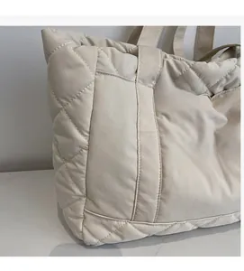 Close-up of beige quilted tote bag featuring large diamond stitching and white embroidery