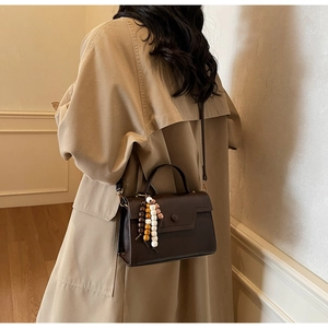 Détail d'un sac à main marron foncé avec perles et bandoulière porté avec un trench-coat chic