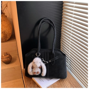 Detail of black suede shoulder bag with metal eyelets and a plush rabbit charm