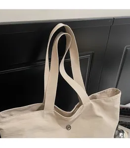 Detail of a beige tote bag featuring a comfortable wide strap and a metal GM logo button