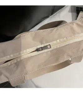 Detailed close-up of smooth metal zipper and durable strap on a beige tote bag