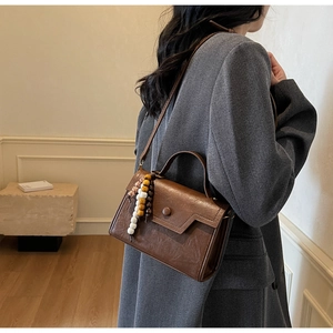 Détail du sac bandoulière vintage en cuir marron avec breloque en perles de bois