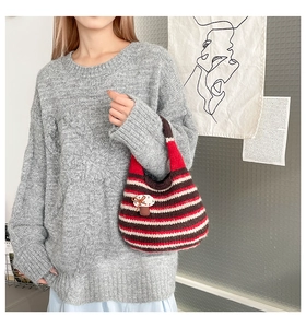 Detail of knit striped bucket bag with mushroom charm paired with a cable knit sweater