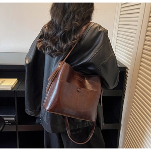 Detailed side view of a vintage brown leather bucket bag worn by a model for daily commute