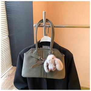Olive green tote bag with white plush rabbit charm hanging on a blazer
