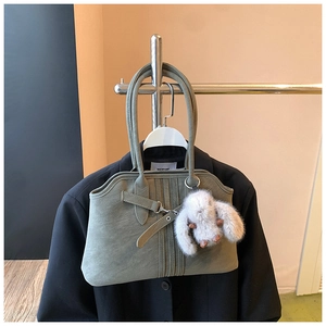 Detail of sage green leather tote bag with belt buckle and plush rabbit keychain