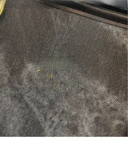 Detail of dark grey twill fabric texture with black leather trim and gold metal rivet