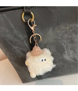 Detail of cream plush monster charm with pink knit hat and gold clasp on a black bag