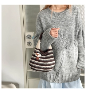 Detail of hand-woven striped bucket bag with mushroom ornament in a cozy knit style
