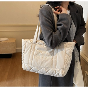 Quilted off-white tote bag with diamond stitching and embroidery shown on model shoulder
