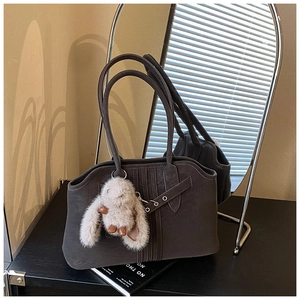 Detail of dark brown tote bag featuring suede texture and plush bunny charm accessory