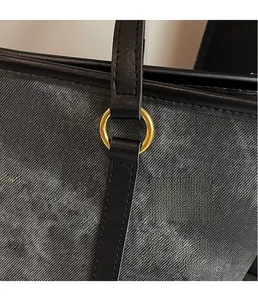 Close-up of golden hardware ring and leather strap on a grey denim tote bag