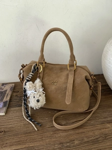 Sac Boston en daim marron avec charm lapin blanc sur une surface en bois vintage