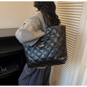 Détail du motif matelassé à losanges et logo métallique sur un grand sac noir