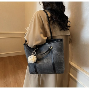 Detail of grey marbled tote bag with plush charm and black leather straps for women