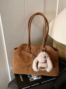 Caramel brown suede tote bag with decorative buckle and plush rabbit charm on books