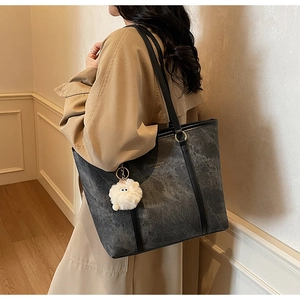 Model showing dark gray marble tote bag with long black handles and a white plush charm
