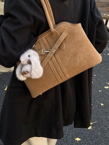 Brown vintage suede tote bag with plush bunny charm worn by model in a street setting