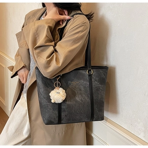Detail of grey textured tote bag with gold hardware and a cute white plush charm