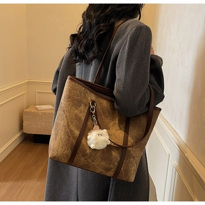 Detail of a brown textured leather tote bag with a white fluffy monster charm accessory