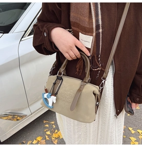 Detail view of beige Boston bag with brown handles and a blue horse charm in outdoor setting