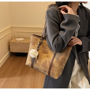 Detail of dark brown leather tote bag with soft plush ball charm on a shoulder strap
